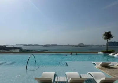 a large swimming pool with chairs and a body of water at Bright and cozy 1BD apartment on the Beachfront in Dubai