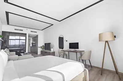 a white bedroom with a bed and a living room at ALiving Luxury Studio I Nicholas Residence, JVC in Dubai