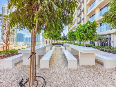 a park with white benches and trees in front of a building at Radiant 1BR in Burj Royale - Downtown Dubai in Dubai