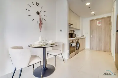 a kitchen with a table and chairs and a clock on the wall at Sleek Studio at UNA Town Square Dubailand by Deluxe Holiday Homes in Dubai