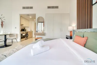 a bedroom with a large white bed and a kitchen at Sleek Studio at UNA Town Square Dubailand by Deluxe Holiday Homes in Dubai