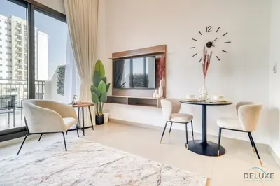 a living room with a table and chairs and a clock at Sleek Studio at UNA Town Square Dubailand by Deluxe Holiday Homes in Dubai