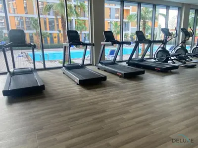 a gym with a row of treadmills and a pool at Incredible Studio at Mesk 1 Midtown Dubai Production City by Deluxe Holiday Homes in Dubai