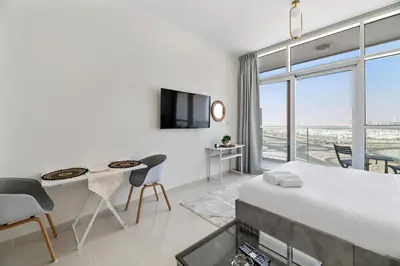 a white room with a bed and a table and chairs at Luxurious - Studio - Damac Hills - Pool & Gym in Dubai