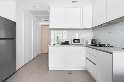 a white kitchen with white cabinets and a refrigerator at Silkhaus new furnished studio in JVC, Luma 21 in Dubai