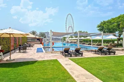 a swimming pool with chairs and a ferris wheel in the background at Beachfront 1 Bed with Full JBR View in Dubai