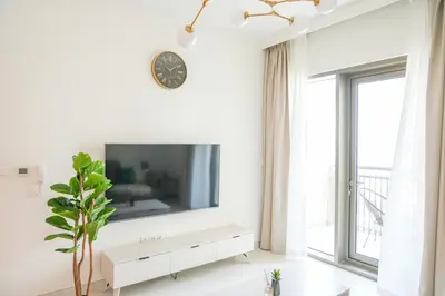a white living room with a large tv on a wall at Elegant Apartment With Balcony Amidst Vibrant Area in Dubai