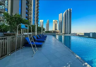 a swimming pool with blue chairs on a building at Elegant Apartment With Balcony Amidst Vibrant Area in Dubai