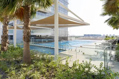 a building with a swimming pool next to a palm tree at Opulent Studio at Carson C DAMAC Hills Dubailand by Deluxe Holiday Homes in Dubai