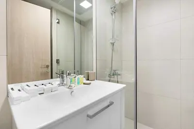 a white bathroom with a sink and a shower at Silkhaus new studio in JVC with queen Bed in Dubai