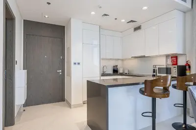 a kitchen with white cabinets and a counter and chairs at Fully Furnished I Lagoons View I District One in Dubai