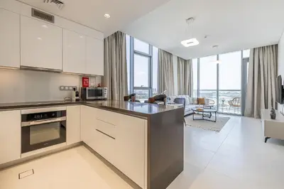 a kitchen with white cabinets and a living room at Fully Furnished I Lagoons View I District One in Dubai
