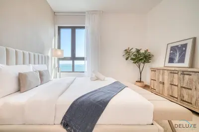 a white bedroom with a large bed and a window at Luxurious 4BR Penthouse with Assistant Room and a Sweeping Balcony Showcasing Burj Khalifa and Sea Views, Le Pont, La Mer by Deluxe Holiday Homes in Dubai