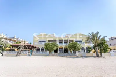 a large white building on the beach with palm trees at Staycae Palm Jumeirah Villa in Dubai