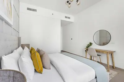 a bedroom with a large white bed with yellow pillows at Silkhaus modern 1BDR in Belgravia Heights with pool & gym in Dubai