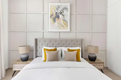 a white bedroom with a large bed with two lamps at Silkhaus modern 1BDR in Belgravia Heights with pool & gym in Dubai