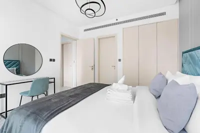 a white bedroom with a large bed and a mirror at Silkhaus chic 1BDR in west avenue with Pool & gym access in Dubai