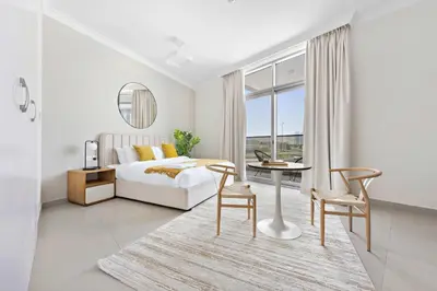 a white bedroom with a bed and a table and chairs at Silkhaus spacious studio in Art Gardens with gym & pool access in Dubai