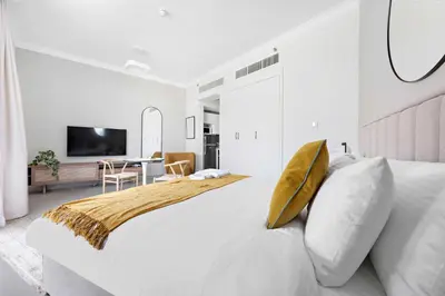 a white bedroom with a large bed with a yellow pillow at Silkhaus spacious studio in Art Gardens with gym & pool access in Dubai