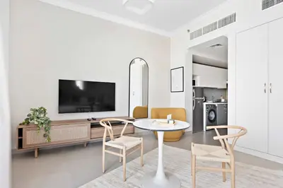 a living room with a table and chairs and a tv at Silkhaus spacious studio in Art Gardens with gym & pool access in Dubai
