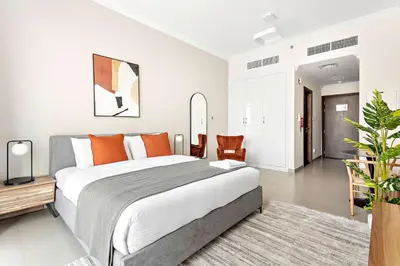 a bedroom with a large bed with orange pillows at Silkhaus furnished studio in Art Gardens with pool access in Dubai