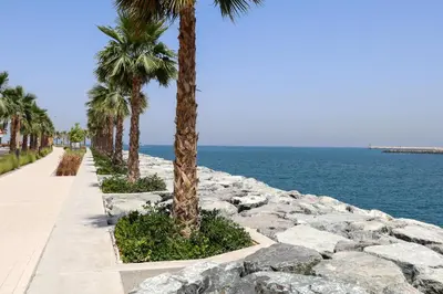 a sidewalk with palm trees next to the ocean at HiGuests - Stylish Waterfront Retreat With Balcony in La Mer in Dubai