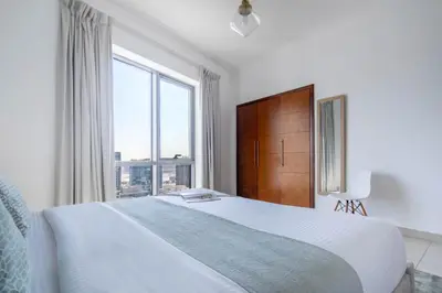 a white bedroom with a large bed and a large window at Frank Porter - South Ridge 6 in Dubai