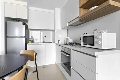 a white kitchen with a microwave and a table at Silkhaus lavish 1BDR in new tower with pool & gym access in Dubai
