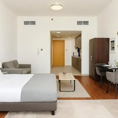 a bedroom with a bed and a table and a kitchen at Cozy Apartment in Jumeirah Village Circle, Dubai. in Dubai