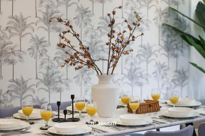 a table with a vase of flowers and glasses of orange juice at Manzil - Luxury 3BR Villa w/ maid room, Full Burj & Fountain view in Dubai