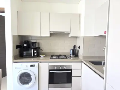 a kitchen with white cabinets and a washer and dryer at Sleek and Stylish 2-Bedroom Apartment in Dubai