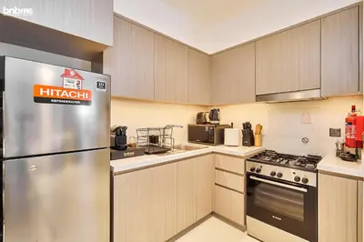 a kitchen with wooden cabinets and a stainless steel refrigerator at bnbme - Luxury 1BR Apt w Burj Khalifa Views Pool Gym & Prime Location Near Dubai Mall in Dubai