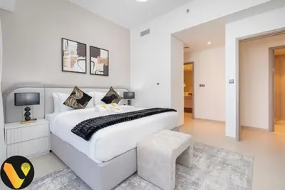 a white bedroom with a large bed and a stool at Vogue Downtown Act Two near Burj Khalifa and Dubai Mall, Three Bedroom Plus Kids room Apartment with Balcony and Burj Khalifa View, Access to all Amenities in Dubai