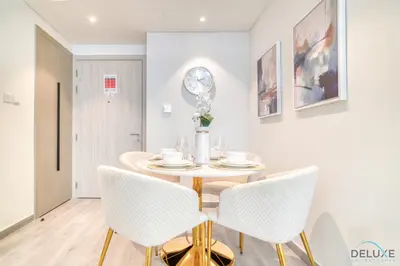 a dining room with a table and chairs and a clock on the wall at Polished 1BR at Noor 1 Midtown Dubai Production City by Deluxe Holiday Homes in Dubai