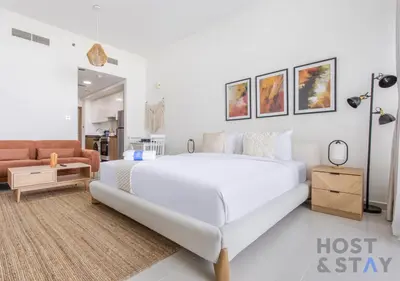 a white bedroom with a large bed and a couch at Studio in Jasmine, Damac Hills - Host & Stay in Dubai