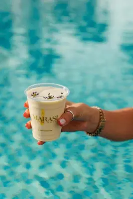 a hand holding a cup with flowers on it next to a pool at Frank Porter - Prive A in Dubai