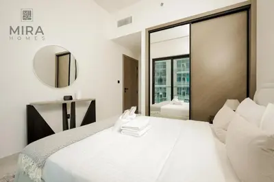 a white bedroom with a large bed and a mirror at Mira Holiday Homes - Serviced 1 bedroom with canal view in Dubai