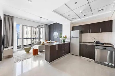 a kitchen with brown cabinets and a living room at Silkhaus in Bay Central Near Metro in Dubai