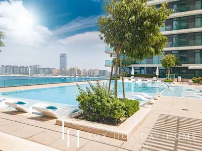 a swimming pool with chairs and a tree on a building at LUX The Beachfront Island View Suite in Dubai