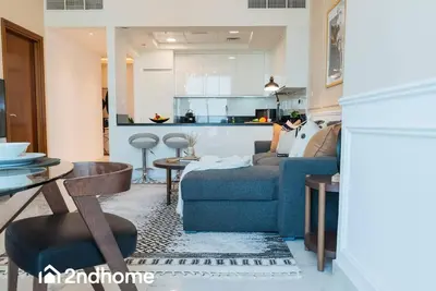 a living room with a blue couch and a kitchen at 2ndHome - Amna Tower, Al Habtoor City in Dubai