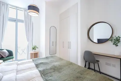 a white bedroom with a large bed and a mirror at Elite LUX Holiday Homes - Serene Golf View Living 1 BHK in Damac Hills, Dubai in Dubai