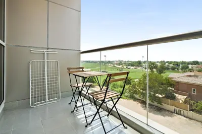 a balcony with a table and chairs and a large window at Stylish Sports City Studio Golf View PoolGym in Dubai
