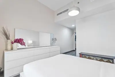 a white bedroom with a white bed and a mirror at ALiving Elegant & Cozy 1BR I Mazaya 11, Liwan in Dubai