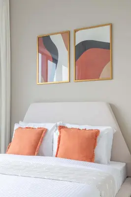 two framed art above a white bed with orange pillows at Frank Porter - Bay Central 1 in Dubai
