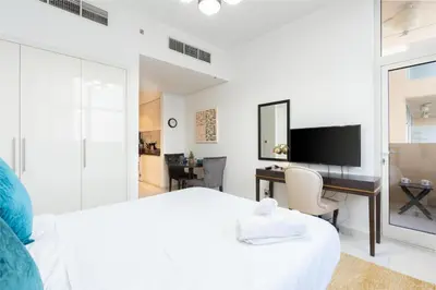 a white bedroom with a desk and a bed at White Sage - Damac Ghalia JVC 35th Floor with Balcony in Dubai