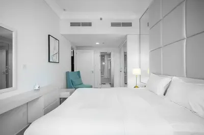 a white bedroom with a large bed and a blue chair at StoneTree - Furnished 1BR in Prime Location in Dubai