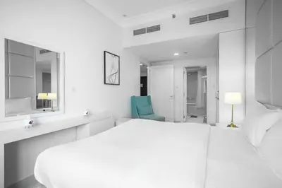 a white bedroom with a white bed and a blue chair at StoneTree - Furnished 1BR in Prime Location in Dubai