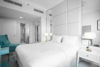 a white bedroom with a large bed and a blue chair at StoneTree - Furnished 1BR in Prime Location in Dubai