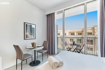 a bedroom with a bed and a balcony with a table and chairs at bnbmehomes - Luma21 in Dubai