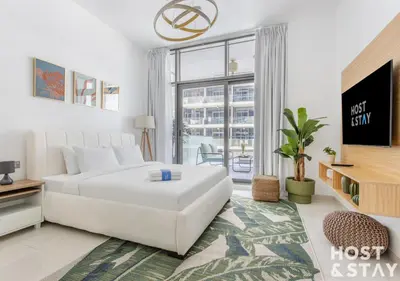 a white bedroom with a bed and a large window at Studio in Loreto 1A, DAMAC Hills - Host & Stay in Dubai